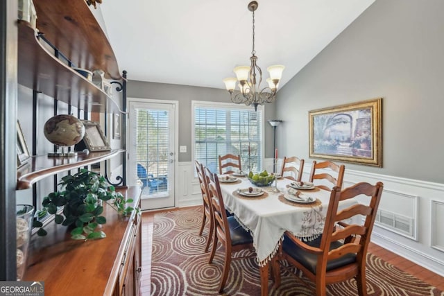 dining area featuring visible vents, a wainscoted wall, lofted ceiling, wood finished floors, and a notable chandelier