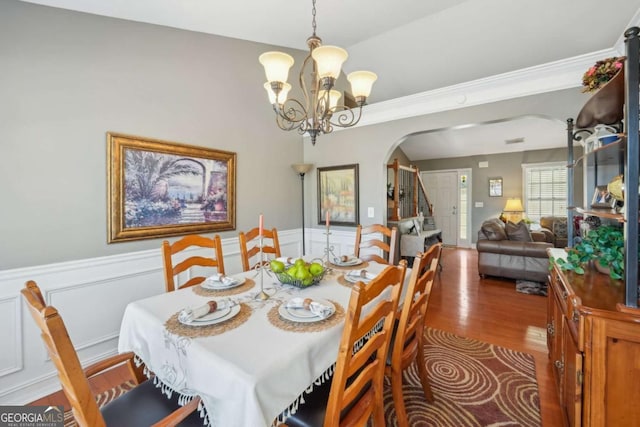 dining area with a chandelier, stairs, wainscoting, wood finished floors, and arched walkways