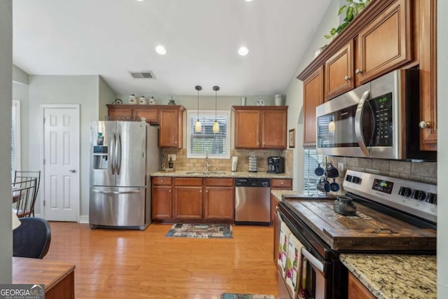 kitchen with a sink, stainless steel appliances, brown cabinetry, and light wood finished floors