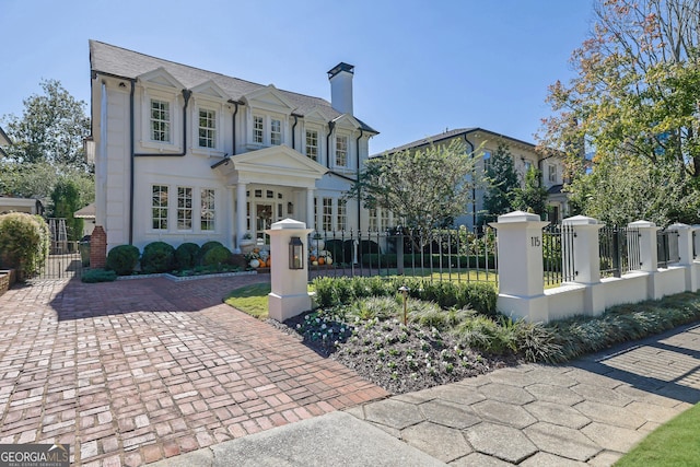 french country style house featuring a fenced front yard, stucco siding, a chimney, and a gate