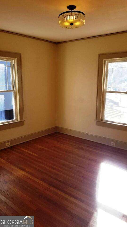 unfurnished room with crown molding, wood finished floors, baseboards, and a wealth of natural light