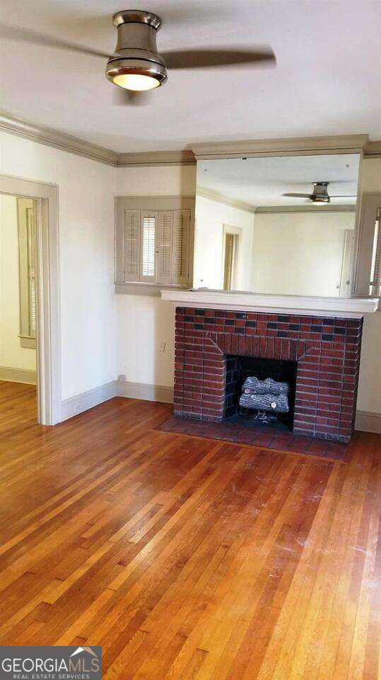 unfurnished living room with baseboards, wood-type flooring, a fireplace, and crown molding