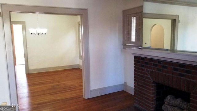 corridor featuring baseboards, a notable chandelier, and wood finished floors