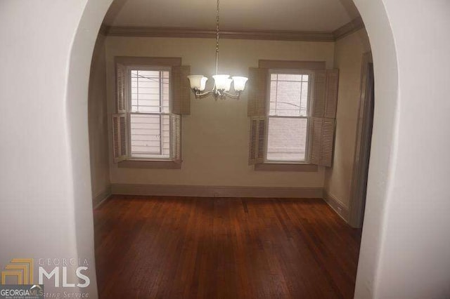 unfurnished dining area with crown molding, wood finished floors, arched walkways, and baseboards