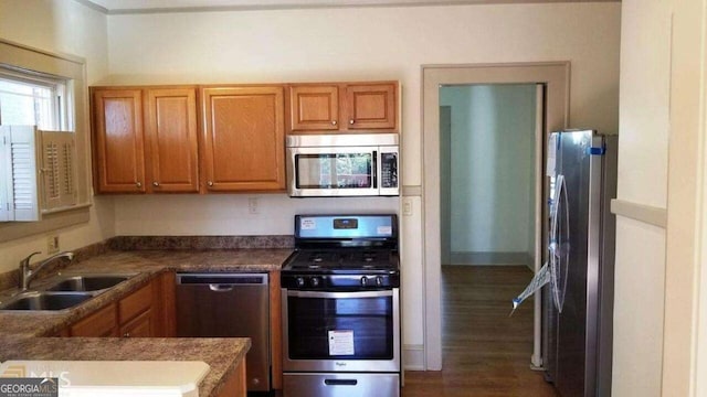 kitchen featuring dark wood-style floors, a sink, stainless steel appliances, dark countertops, and brown cabinets