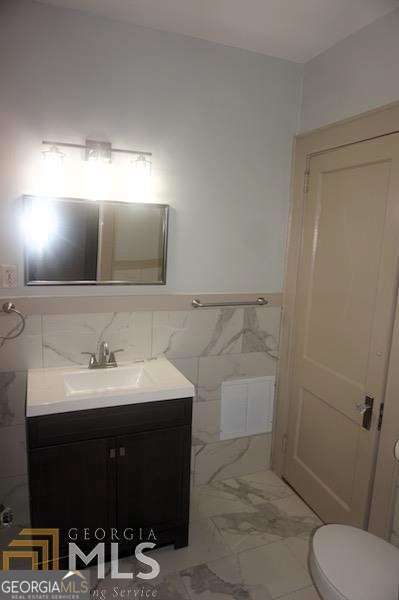 bathroom featuring tile walls, a wainscoted wall, toilet, marble finish floor, and vanity