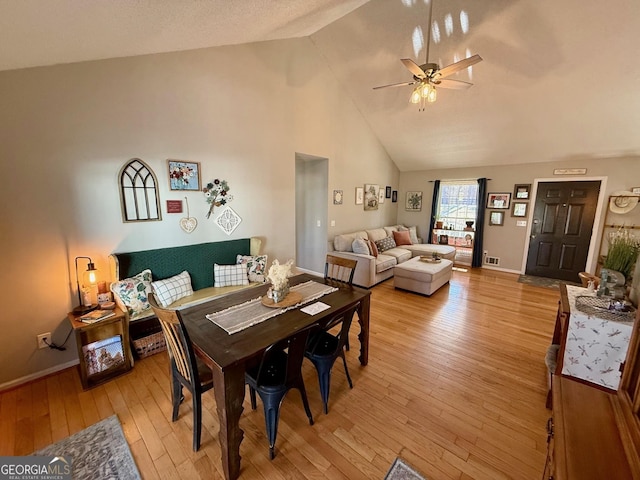 dining room with visible vents, baseboards, ceiling fan, light wood-type flooring, and high vaulted ceiling