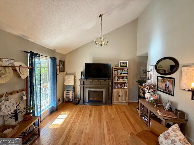 living area featuring light wood finished floors, a fireplace with flush hearth, a textured ceiling, and a notable chandelier