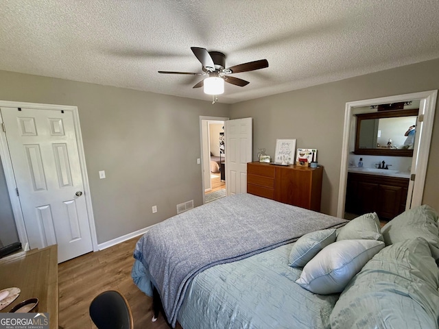 bedroom featuring a sink, visible vents, a textured ceiling, and wood finished floors