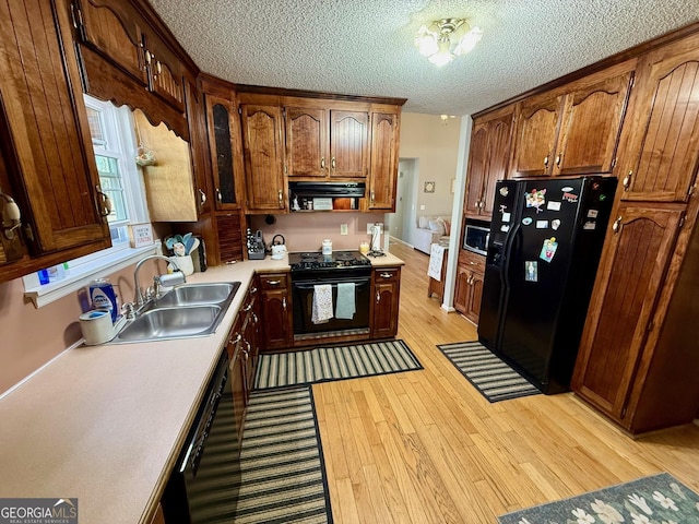 kitchen featuring range hood, a sink, black appliances, light countertops, and light wood-style floors