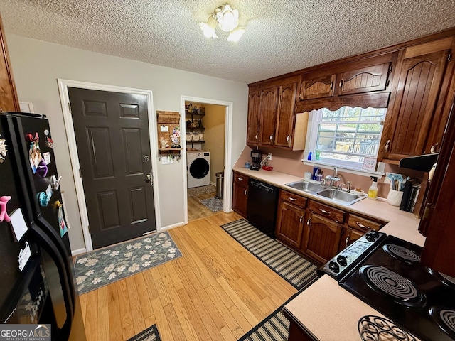 kitchen featuring light wood finished floors, washer / dryer, a sink, light countertops, and black appliances