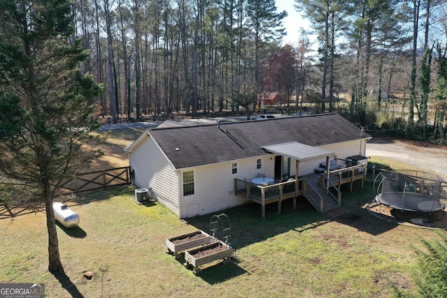 rear view of house featuring a trampoline, fence, a yard, a deck, and a gate