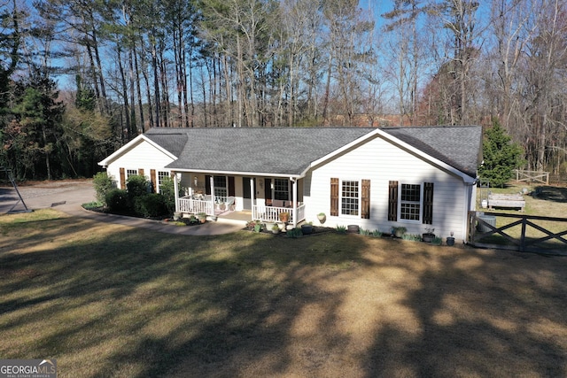 ranch-style home with a porch, a shingled roof, a front yard, and fence