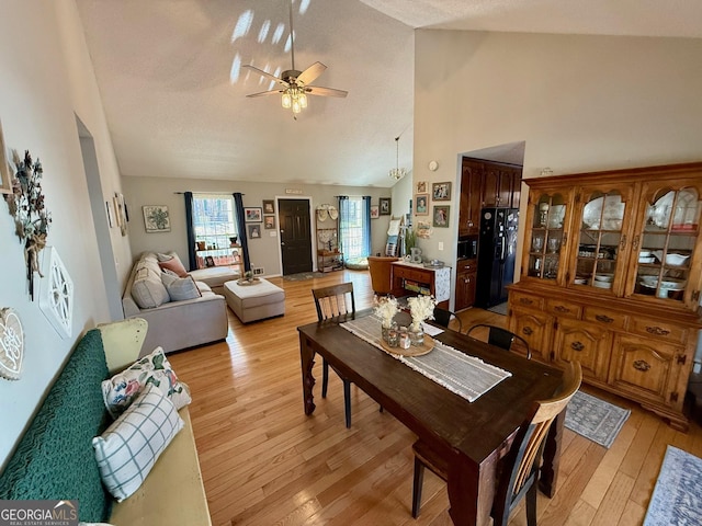 dining area with a ceiling fan, light wood-style floors, and high vaulted ceiling