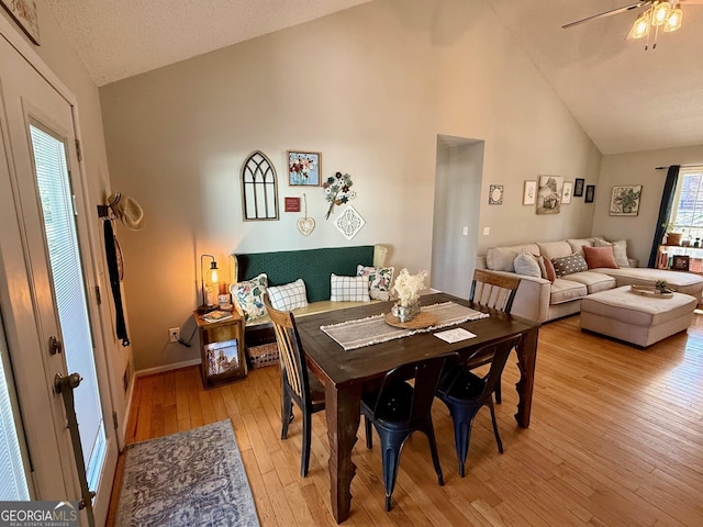 dining room with a ceiling fan, baseboards, light wood finished floors, high vaulted ceiling, and a textured ceiling