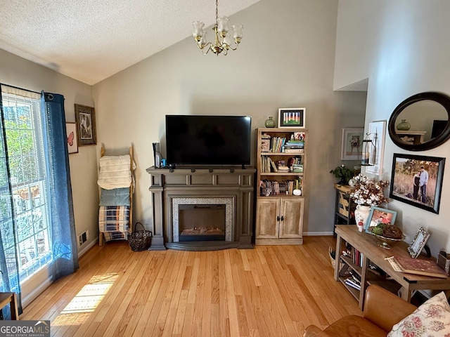 living area with a notable chandelier, a textured ceiling, hardwood / wood-style floors, a high end fireplace, and lofted ceiling