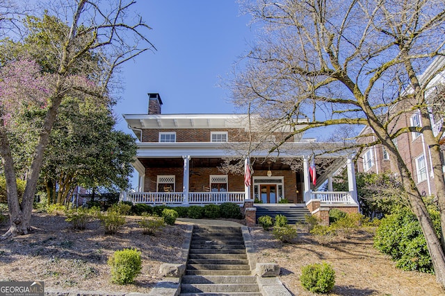 view of front of house featuring a chimney, a porch, french doors, brick siding, and stairs