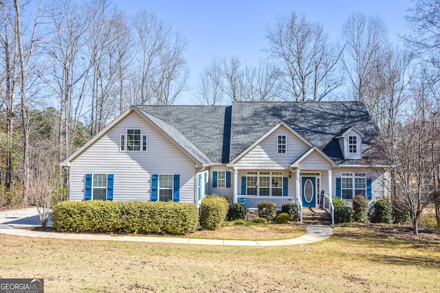 view of front of house with covered porch, a shingled roof, and a front yard