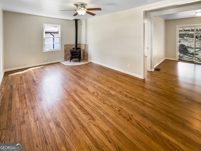 unfurnished living room featuring ceiling fan, baseboards, wood finished floors, and a wood stove