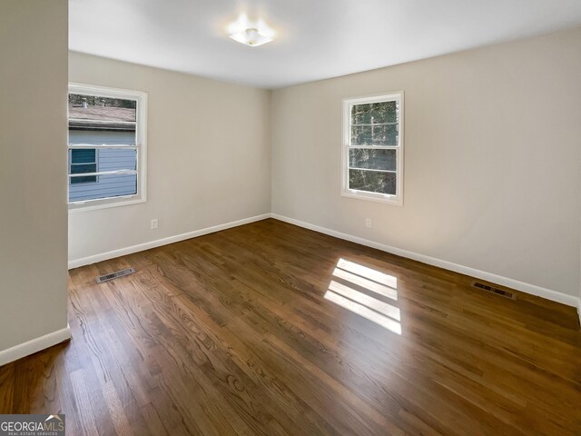 spare room featuring dark wood finished floors, visible vents, and baseboards