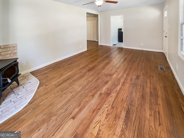 living area featuring visible vents, wood finished floors, baseboards, ceiling fan, and a wood stove