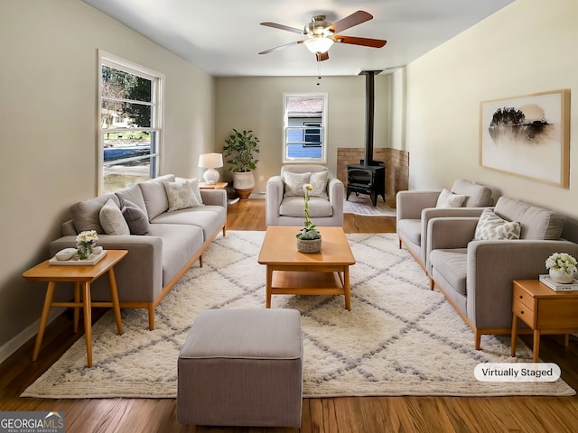 living room featuring a ceiling fan, a wood stove, wood finished floors, and baseboards