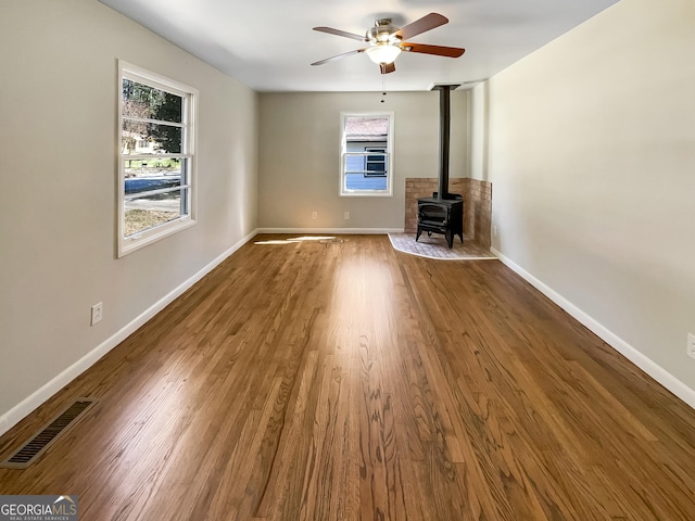 unfurnished living room with visible vents, baseboards, wood finished floors, and a wood stove