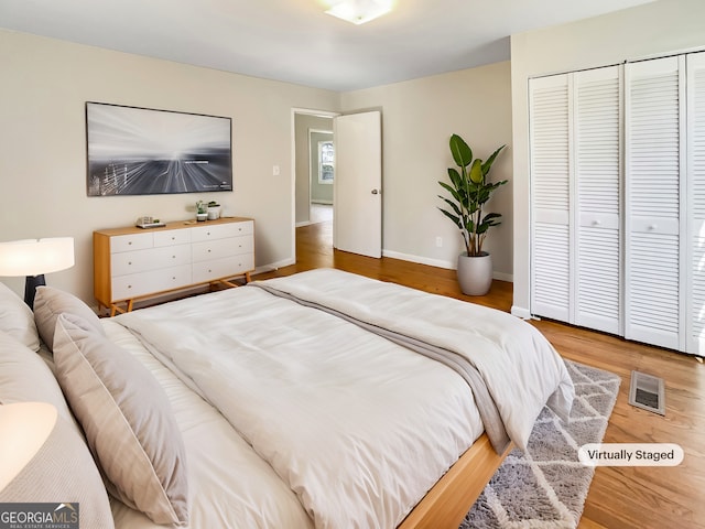 bedroom with a closet, visible vents, baseboards, and wood finished floors