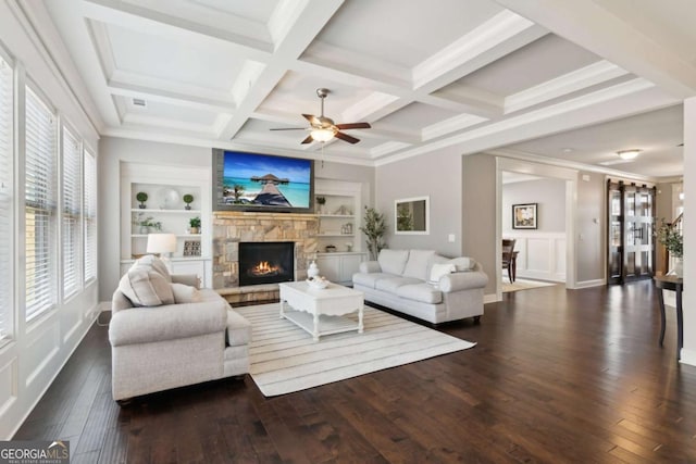 living area with beamed ceiling, built in features, coffered ceiling, dark wood-style floors, and a stone fireplace