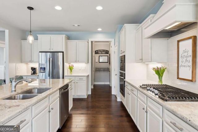 kitchen with premium range hood, white cabinets, stainless steel appliances, and a sink