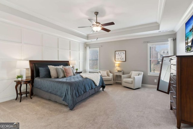 bedroom featuring baseboards, a tray ceiling, light carpet, crown molding, and a decorative wall