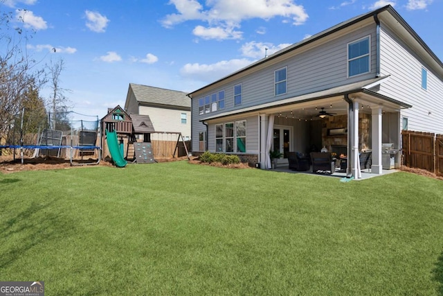 back of property with a yard, a fenced backyard, ceiling fan, a playground, and a trampoline