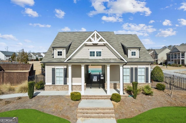 view of front facade with brick siding, covered porch, and fence