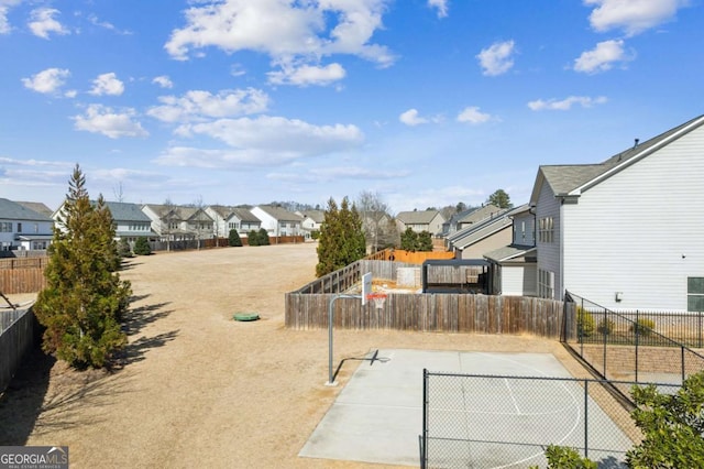 view of basketball court featuring basketball hoop, fence, and a residential view