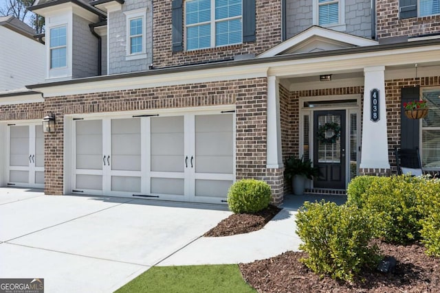 doorway to property with an attached garage, brick siding, and driveway