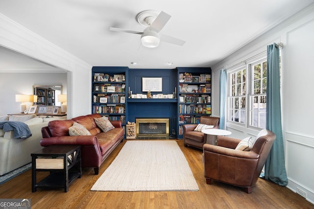 living area featuring a glass covered fireplace, crown molding, wood finished floors, and ceiling fan