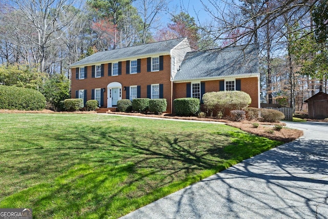 colonial inspired home featuring a front lawn, brick siding, and driveway