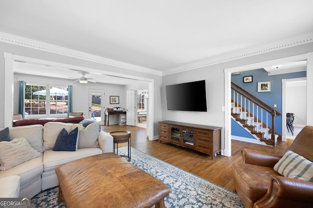 living room with a ceiling fan, wood finished floors, baseboards, ornamental molding, and stairs