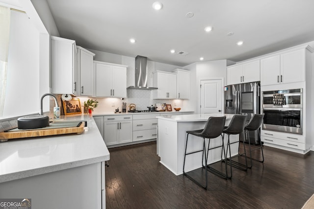 kitchen featuring a center island, recessed lighting, a kitchen bar, and wall chimney range hood