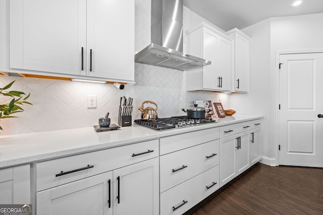 kitchen with white cabinets, wall chimney range hood, dark wood-type flooring, decorative backsplash, and stainless steel gas cooktop