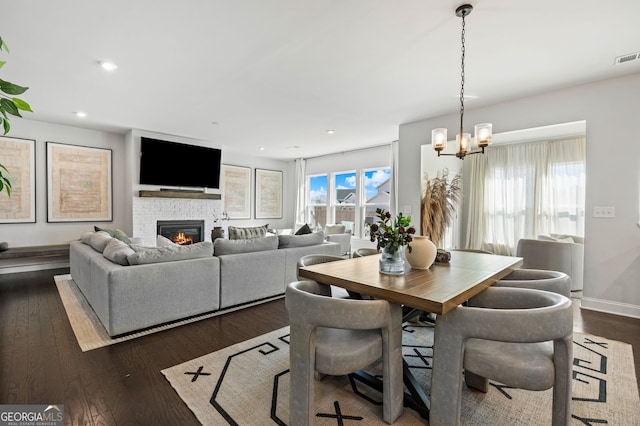 dining space featuring baseboards, recessed lighting, dark wood-type flooring, a glass covered fireplace, and a notable chandelier