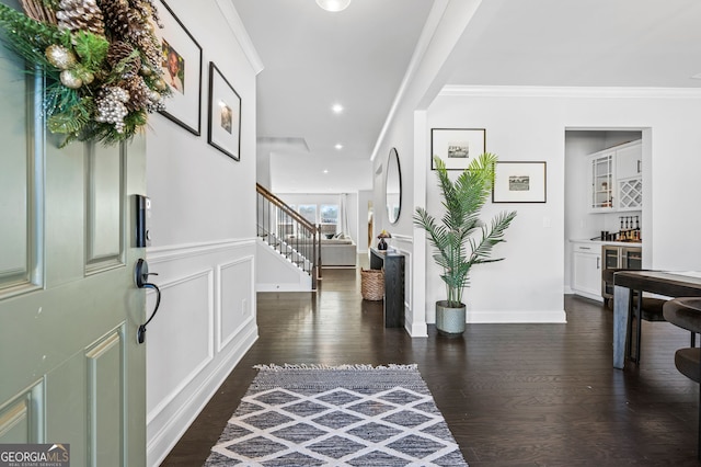 foyer featuring stairway, dark wood-style flooring, ornamental molding, a decorative wall, and indoor bar