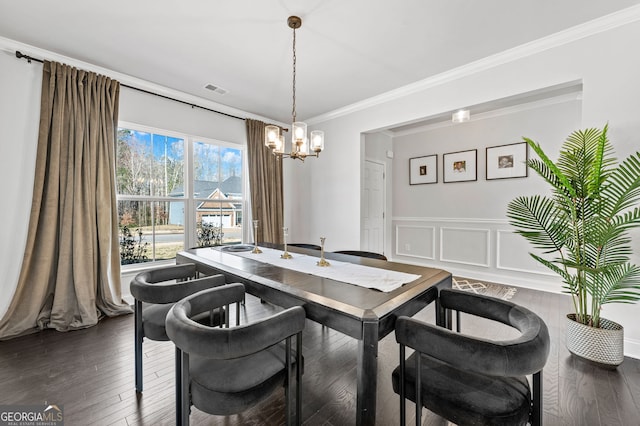 dining area with a wainscoted wall, an inviting chandelier, visible vents, dark wood-type flooring, and crown molding