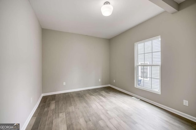 unfurnished room with visible vents, baseboards, beam ceiling, and wood finished floors