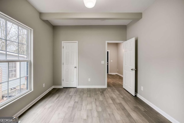 unfurnished bedroom featuring beam ceiling, wood finished floors, and baseboards