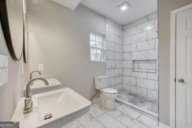 bathroom featuring baseboards, toilet, a tile shower, marble finish floor, and a sink