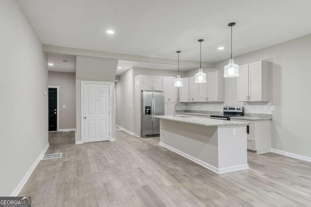 kitchen with visible vents, a kitchen island with sink, stainless steel appliances, light wood finished floors, and decorative backsplash