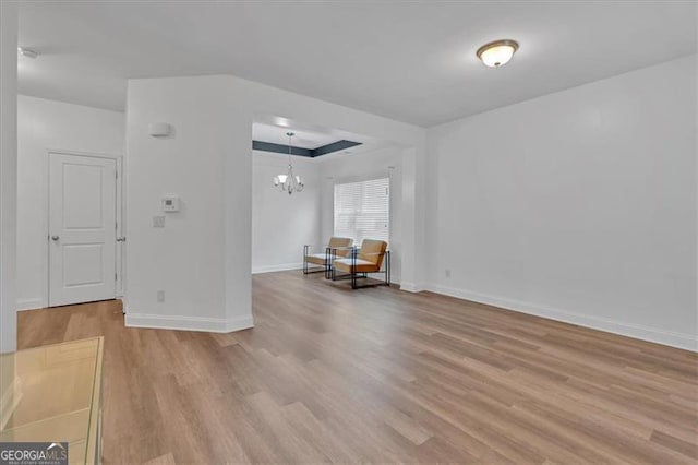 unfurnished room featuring a tray ceiling, light wood-style flooring, baseboards, and a chandelier