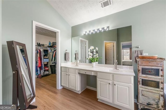 full bath featuring visible vents, lofted ceiling, double vanity, wood finished floors, and a sink