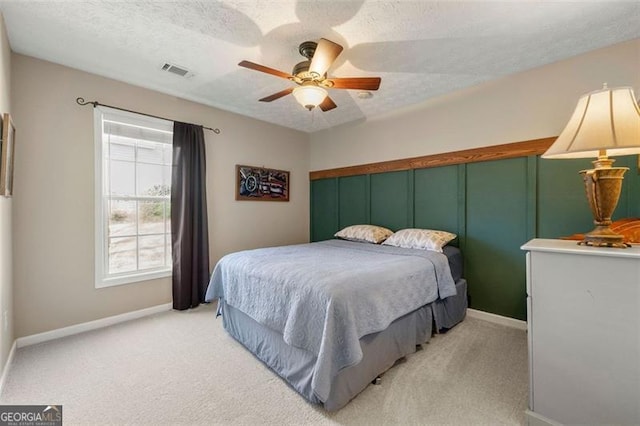 bedroom with a textured ceiling, baseboards, visible vents, and light carpet